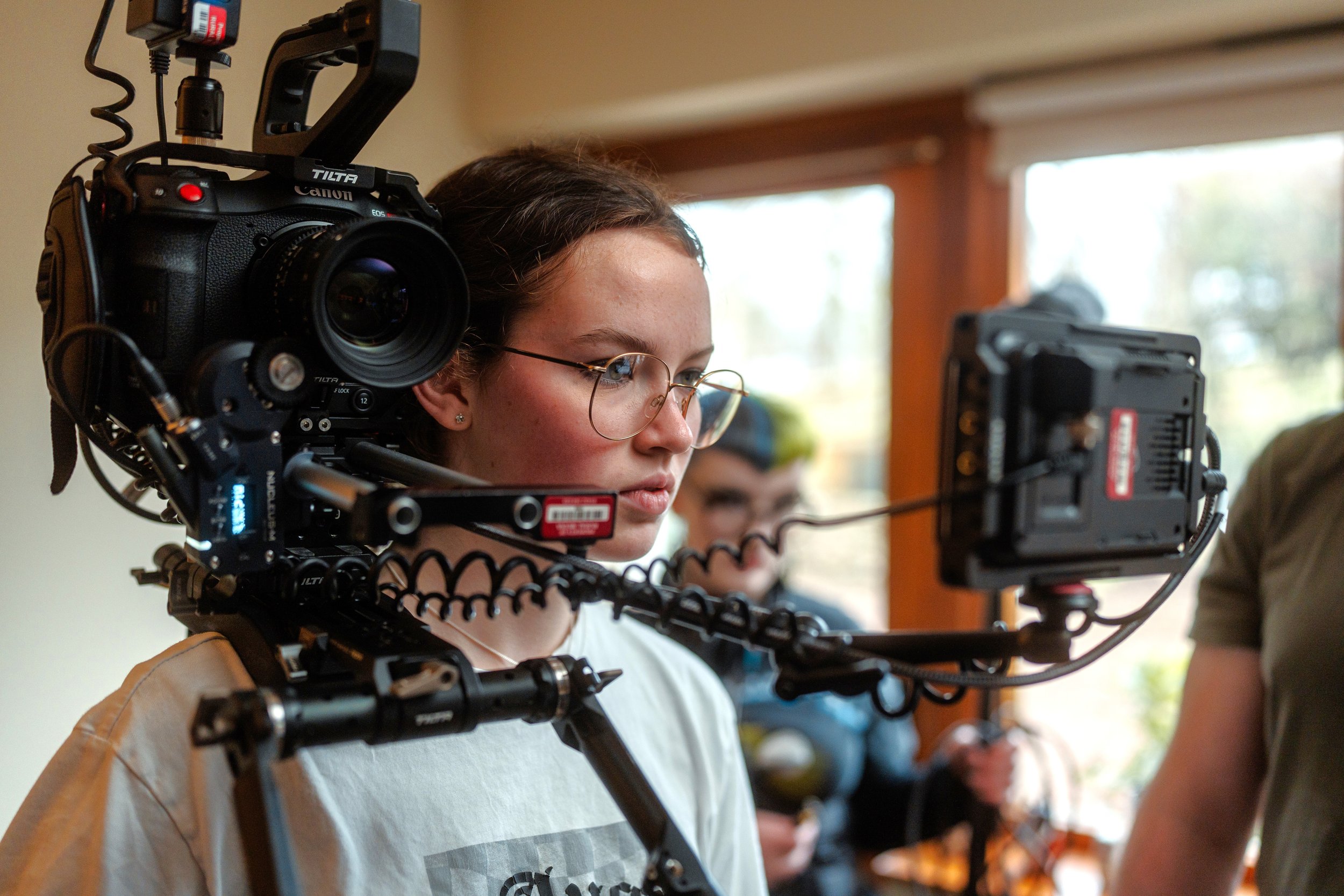 A young BFI Film Academy camera operator with a shoulder-mounted cinema camera, a focus monitor rigged alongside.